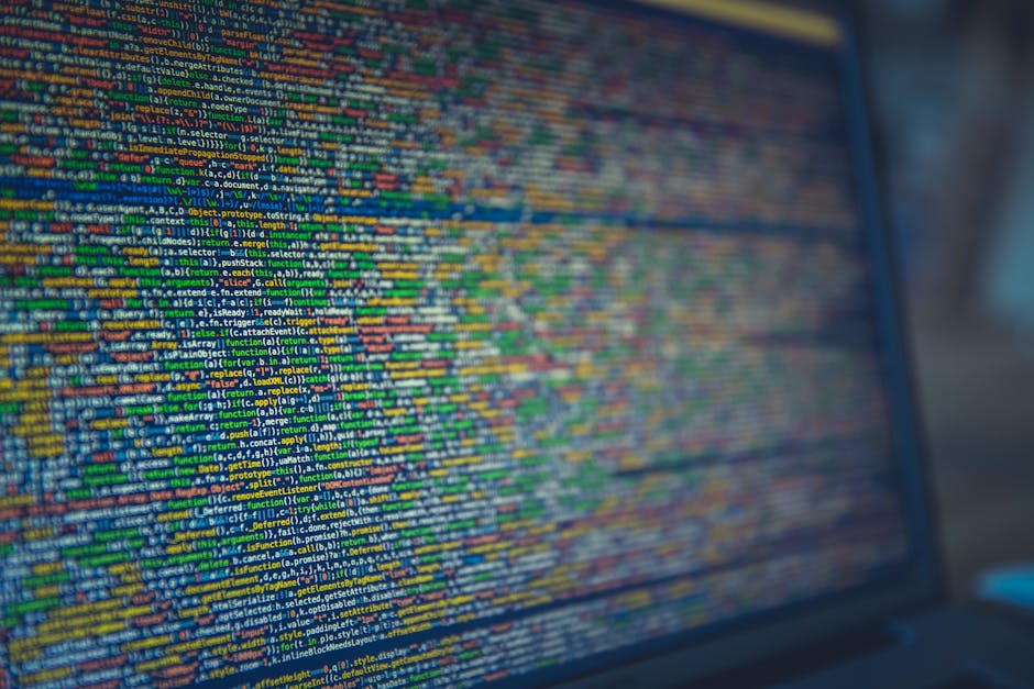 A close-up view of a computer screen displaying lines of HTML code in a dark environment, with syntax highlighting showing tags and text in various colors including green, yellow, and white. The code 